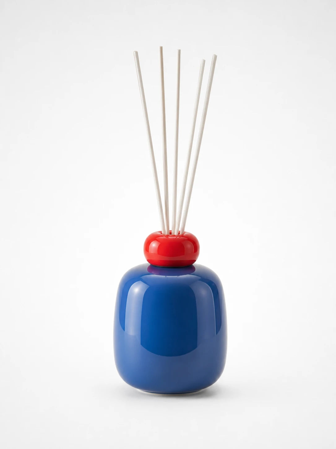 glossy cobalt blue ceramic reed diffuser bottle with a red ring cap holding six white reeds