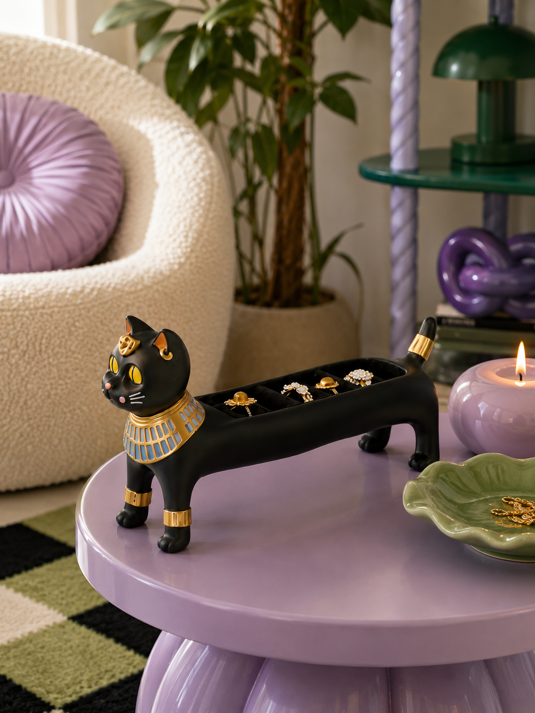 black Egyptian cat ring holder on a lilac side table beside a boucle armchair and a purple candle