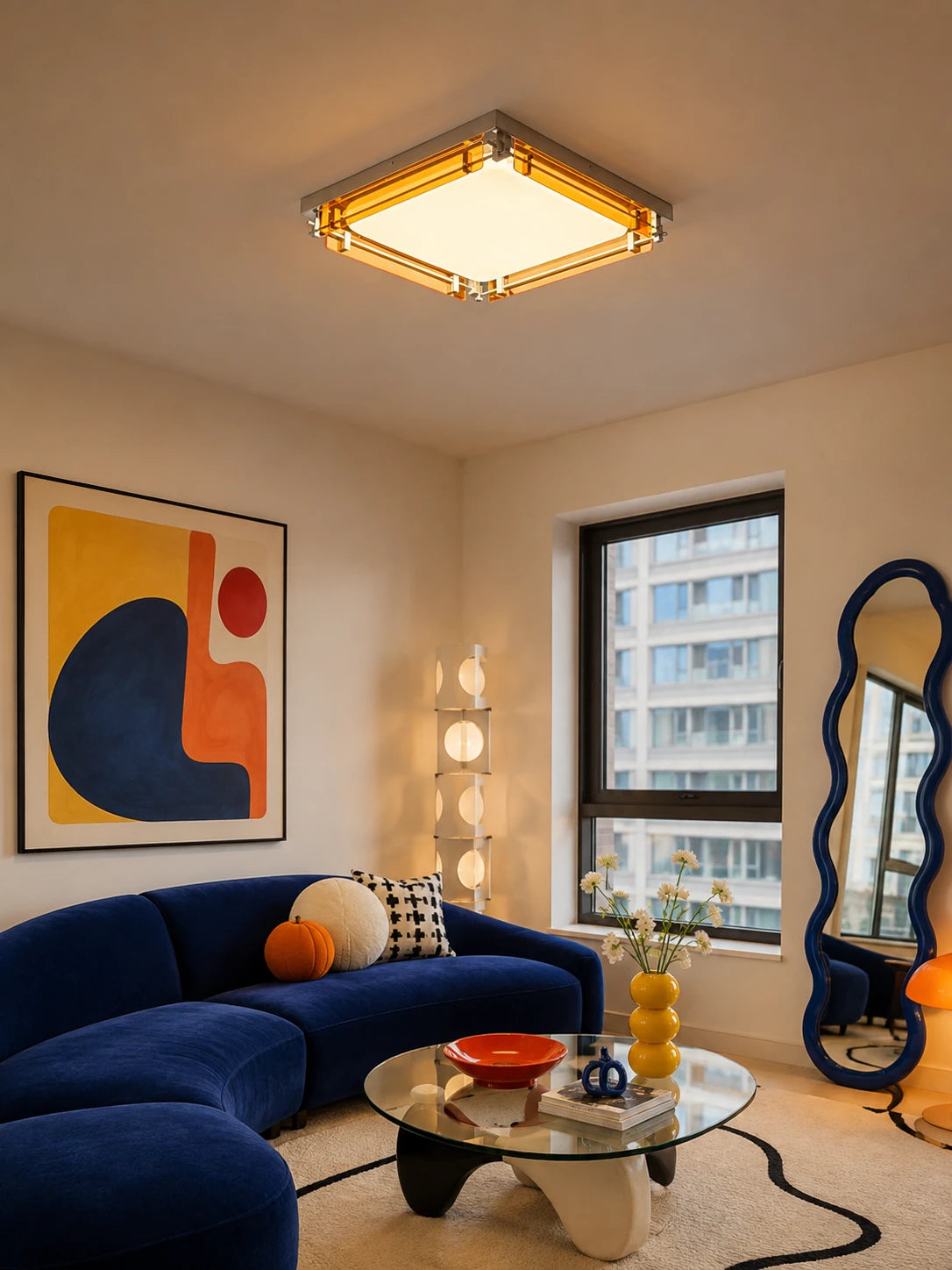 amber acrylic flush mount ceiling light glowing warm above a blue velvet sofa and abstract wall art