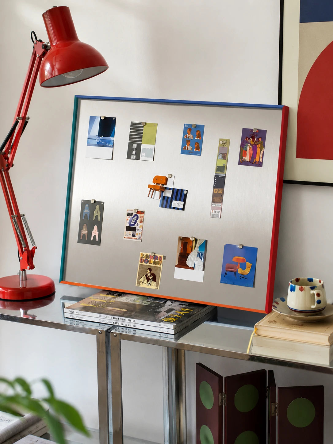multicolor frame magnetic board on a chrome console desk with a red task lamp, pinned with cards
