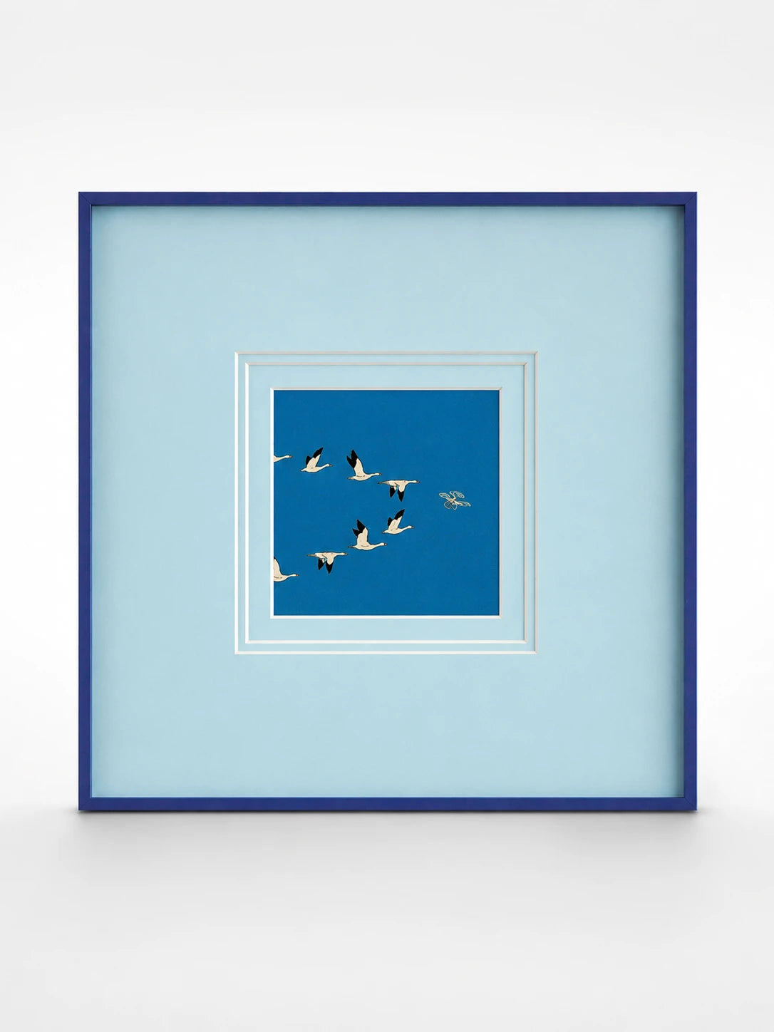 framed canvas print of white geese flying on deep blue, set in a wide pale blue mat with a navy frame