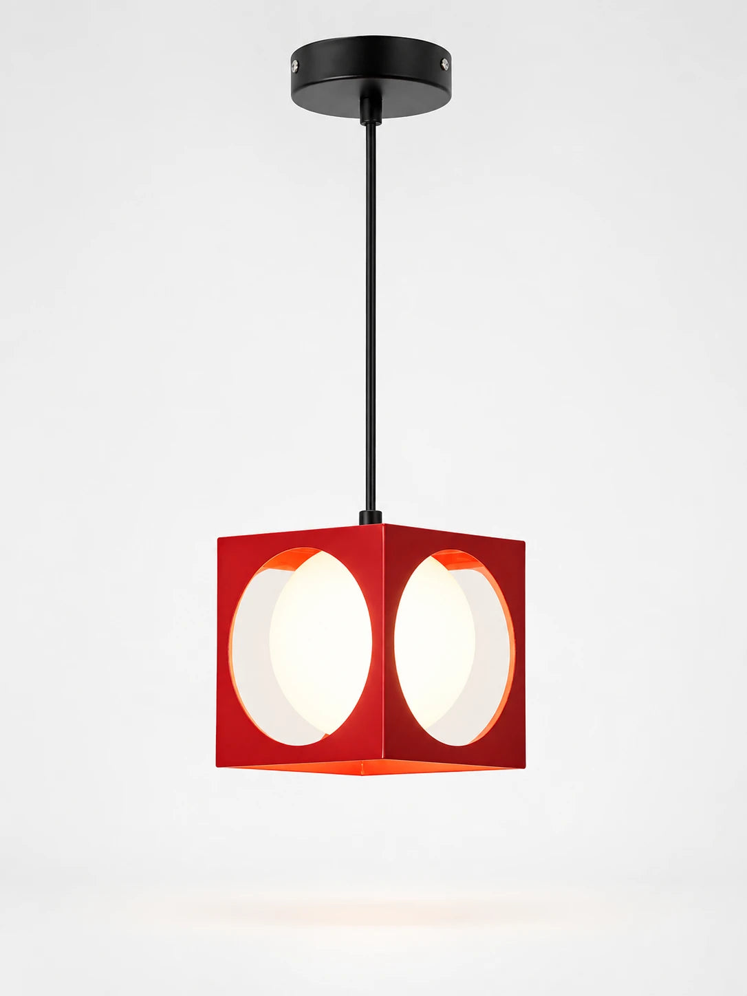 red cube pendant light with circular cutouts revealing a white opal glass globe, hanging from a black cord