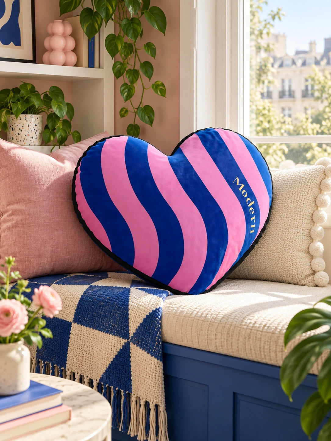 Blue and pink striped heart pillow on a window-seat bench in a sunny nook
