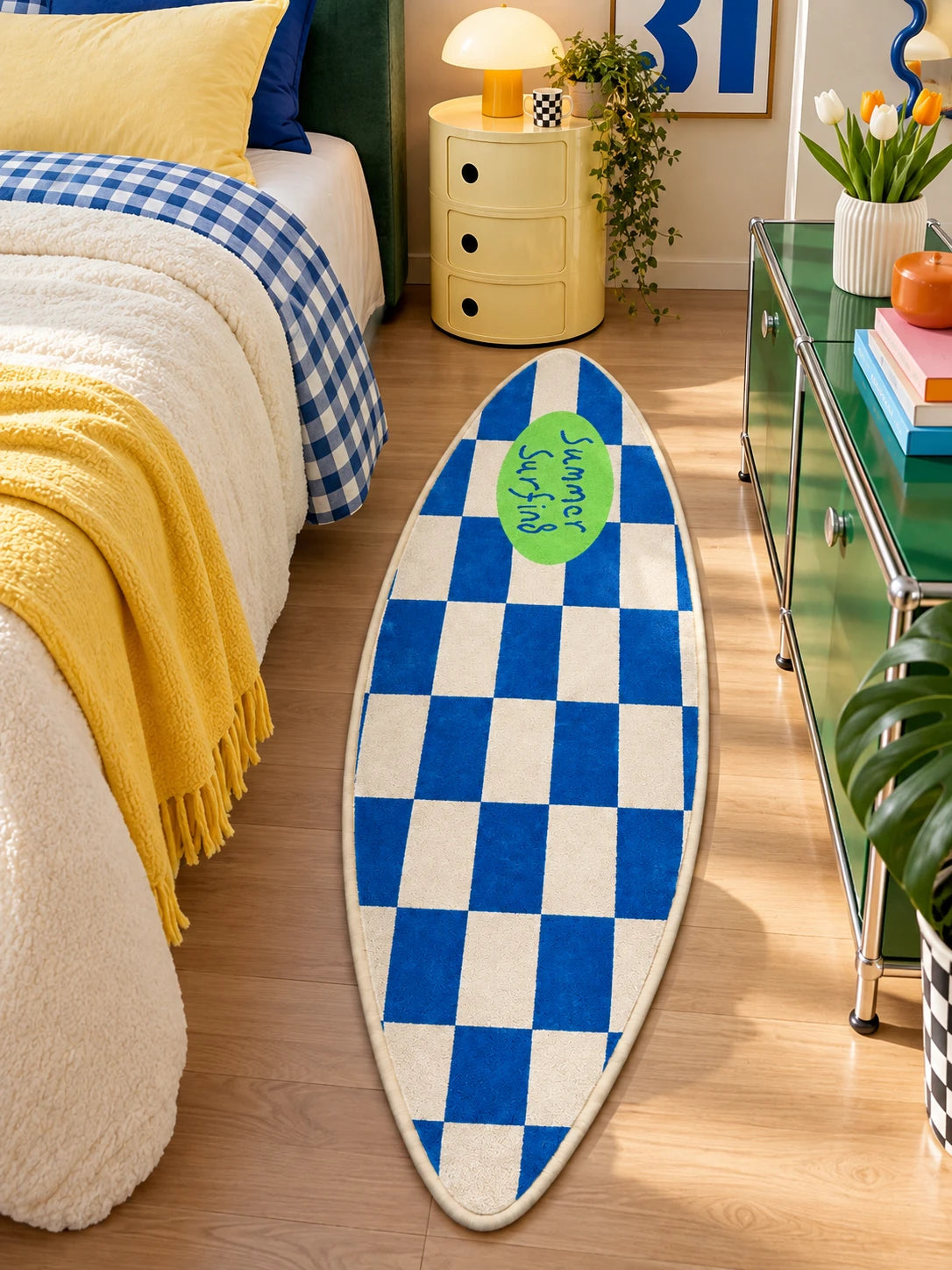 Surfboard rug next to a bed with blue gingham skirt, yellow throw and green glass console