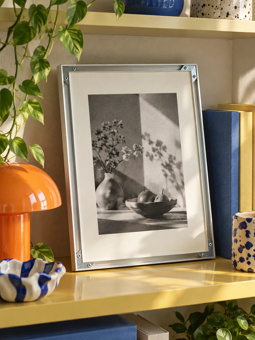 silver aluminum poster frame with black and white still life print leaning on a shelf