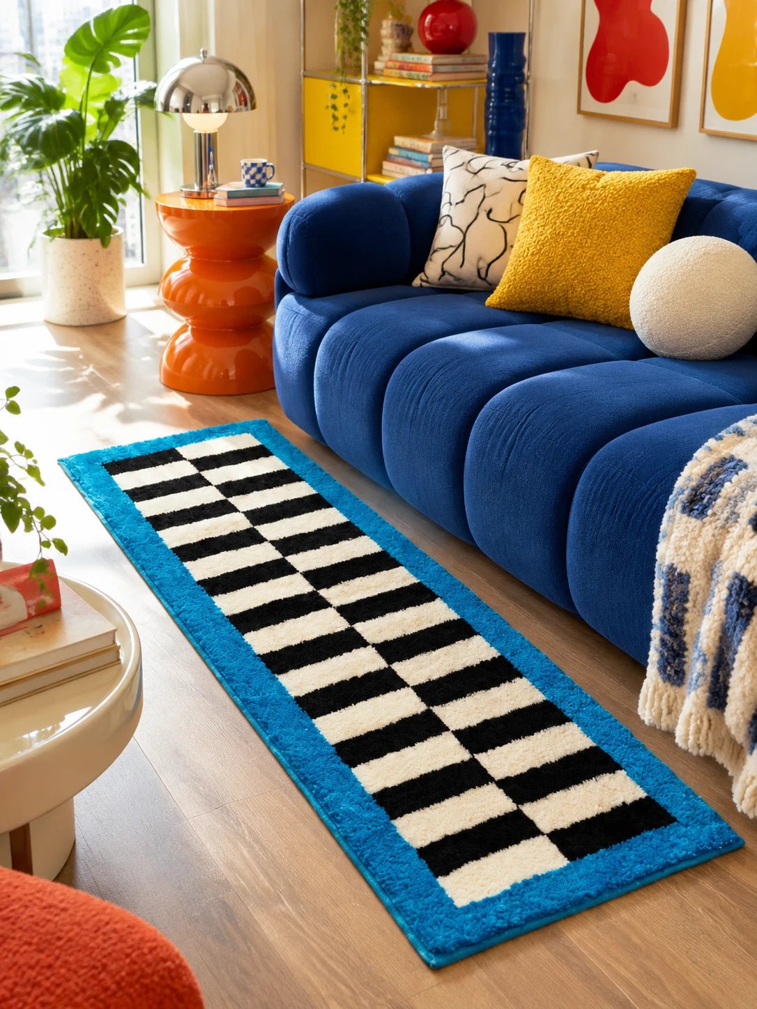 Checkerboard runner rug beside a cobalt channel sofa with an orange side table and a yellow pillow