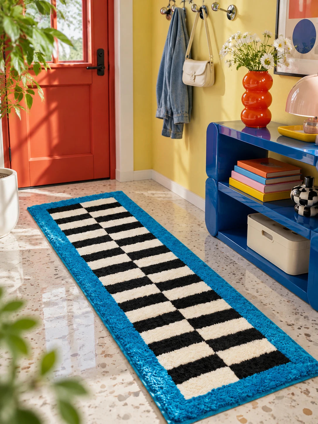 Checkerboard runner rug in a yellow entryway by a red door, a cobalt console and wall hooks