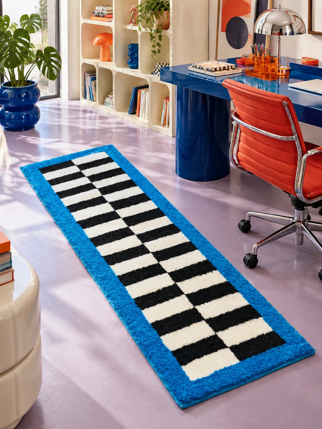 Blue border checkerboard runner on a lilac floor beside a cobalt desk and an orange office chair
