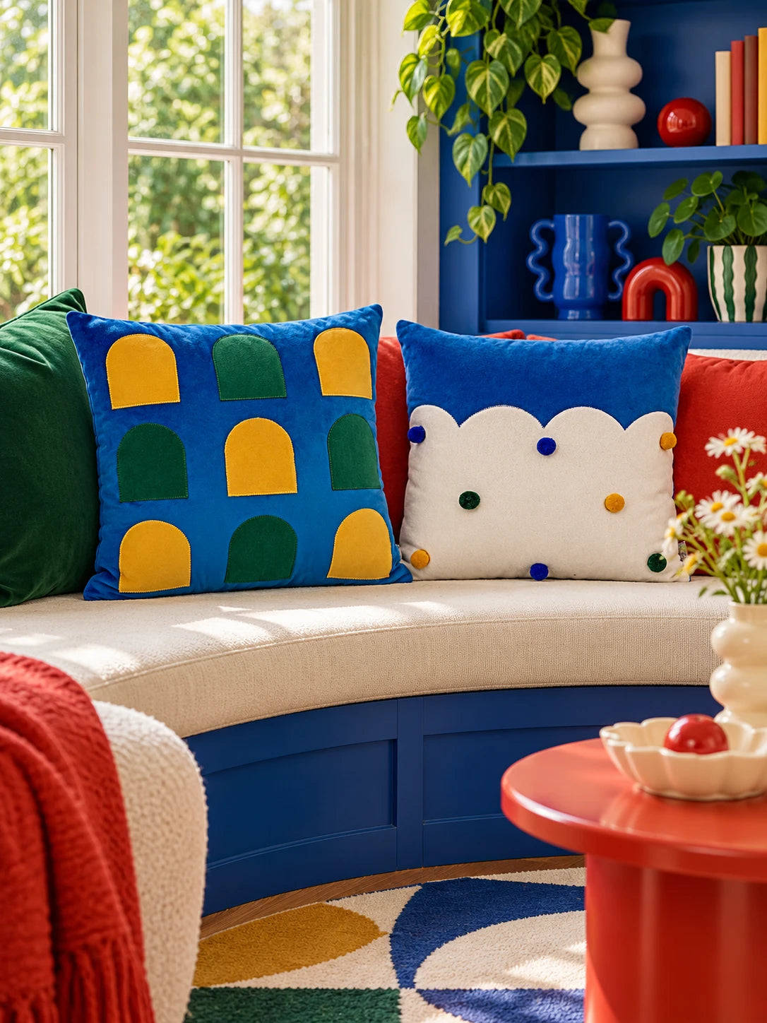 Window-arch and cloud-edge throw pillows on a curved cream window seat with a red side table