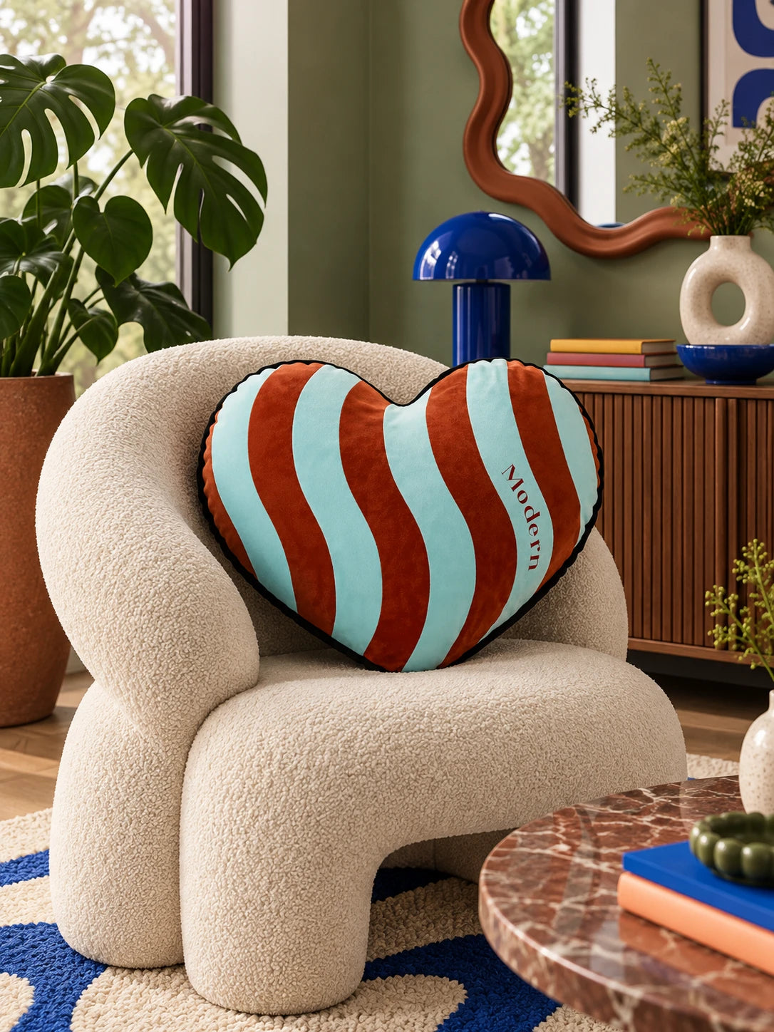 Aqua and rust heart pillow on a cream boucle armchair beside a wavy mirror