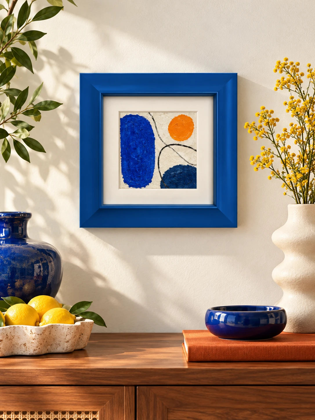 blue wood frame with abstract painting hanging above a walnut sideboard with lemons