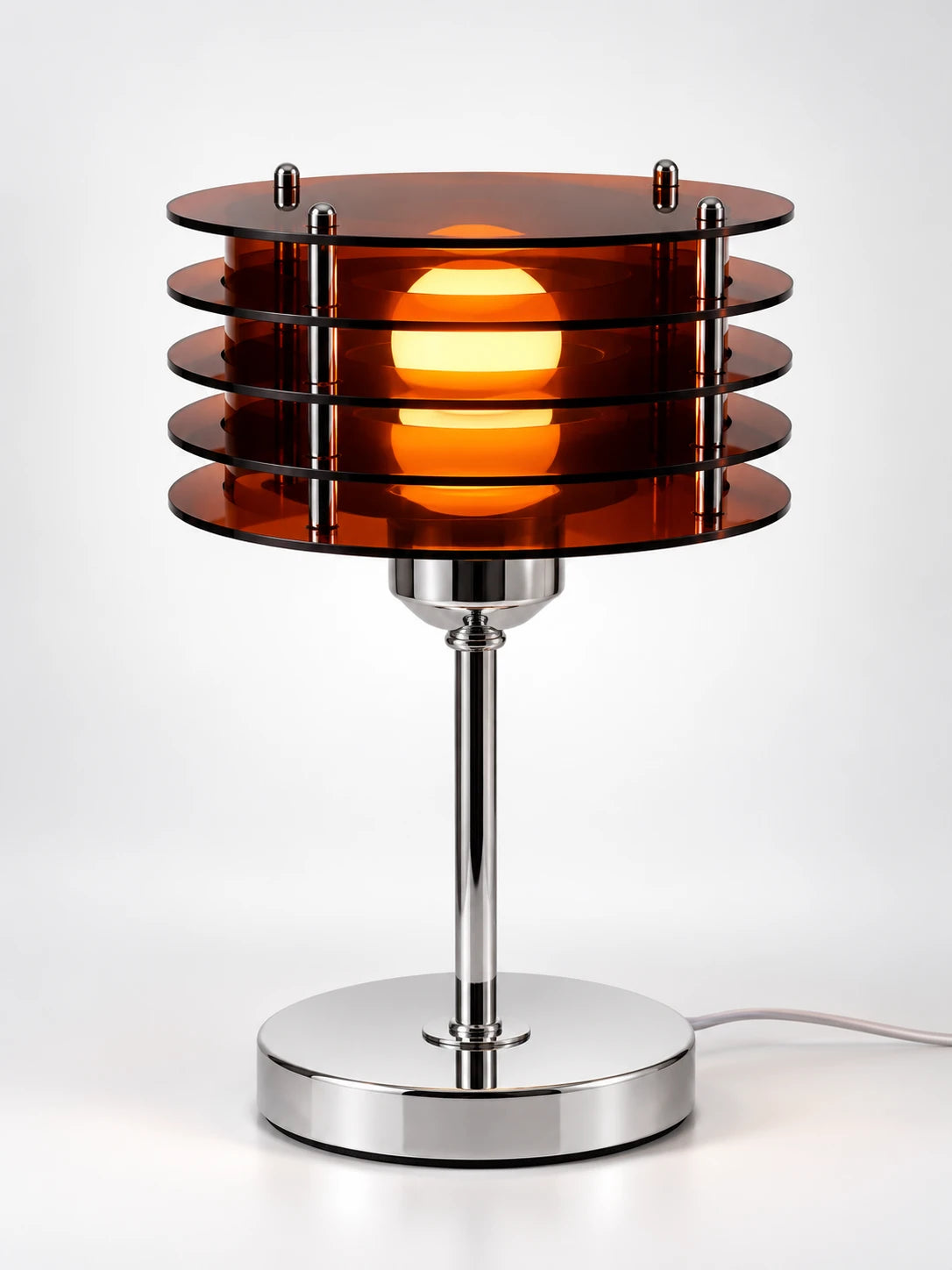 Smoked acrylic disc table lamp with stacked amber discs around a glowing globe bulb on a chrome-look stem, studio shot