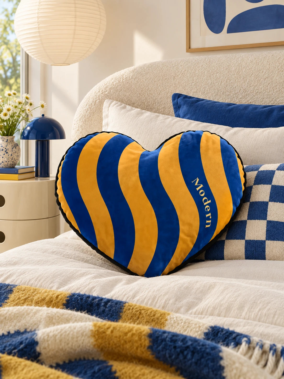 Blue and marigold heart pillow on a cream bed with a checkered blanket