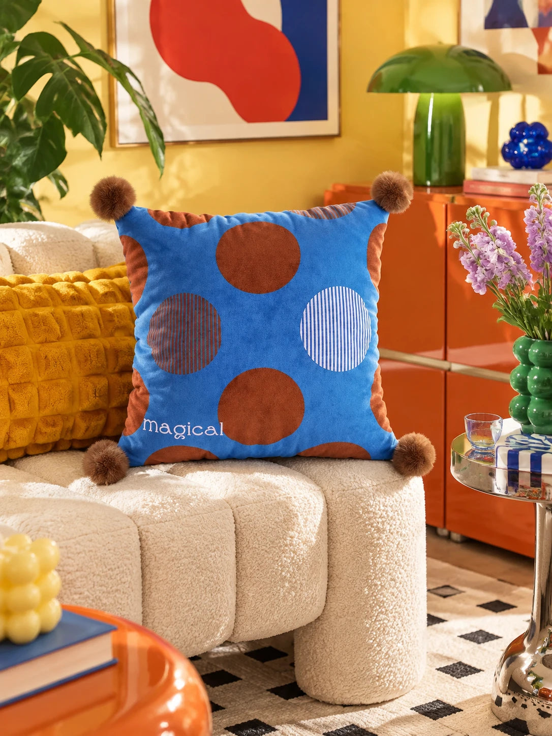 Cobalt and brown dot pompom pillow on a cream boucle sofa in front of an orange sideboard