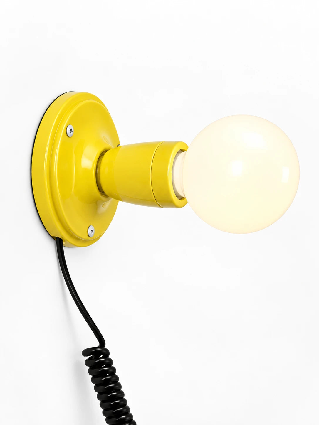 yellow ceramic wall light with an opal globe bulb and coiled black cord, studio shot on white
