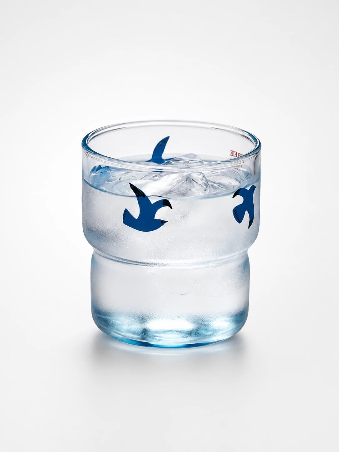 blue-tinted glass tumbler filled with iced water, printed with small flat navy flying-bird shapes