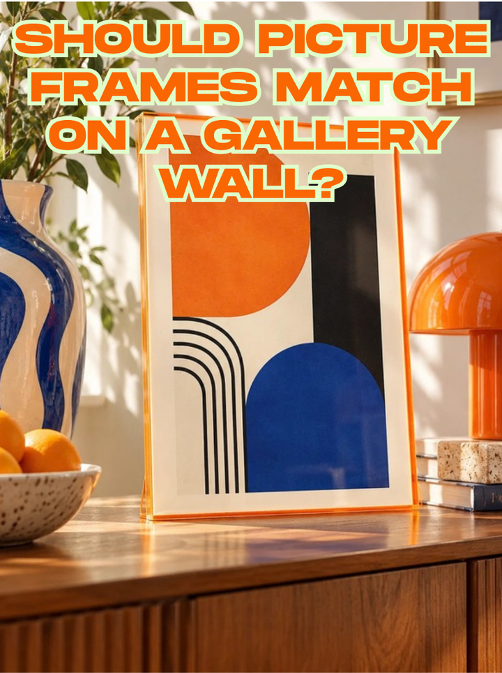 Orange tinted acrylic picture frame with an orange and blue abstract print on a walnut sideboard, with the title Should Picture Frames Match on a Gallery Wall?
