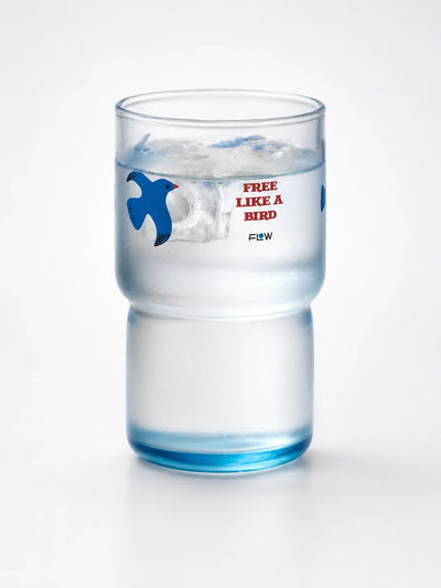 tall blue-tinted glass tumbler with a flying-bird motif and a narrower stepped base, filled with ice water