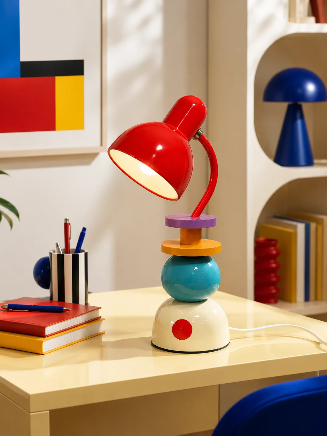 Memphis stacked orb table lamp glowing on a yellow desk beside books and a pen cup