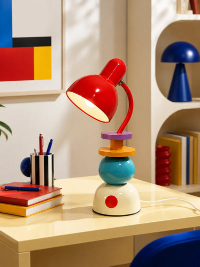 Memphis stacked orb table lamp glowing on a yellow desk beside books and a pen cup