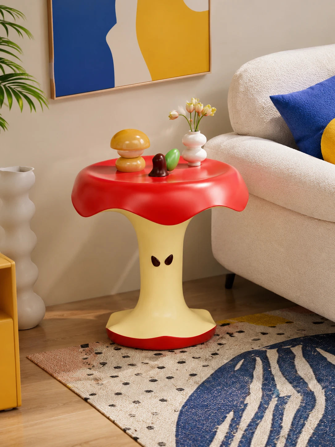 red apple core side table beside a white boucle sofa with tulips and trinkets on its top