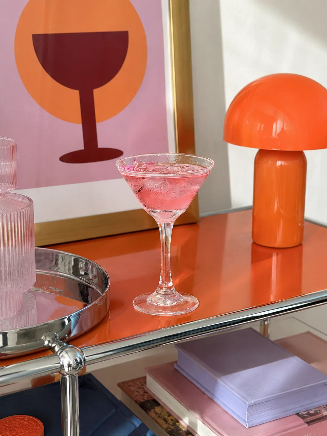 pink cocktail in a clear martini glass on an orange bar cart beside an orange mushroom lamp