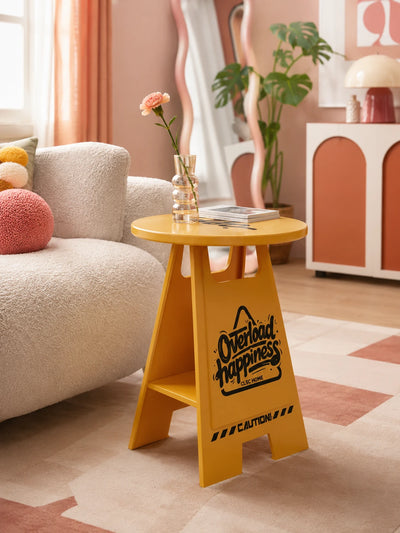 mustard yellow caution-sign side table with black graphics holding a bud vase with a carnation beside a boucle sofa