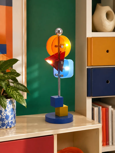 colorful geometric table lamp glowing on a cream shelf against a green wall beside storage boxes