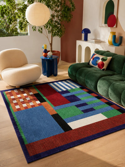 bauhaus style patchwork rug under a glass-walled living room with green channel-tufted sofa