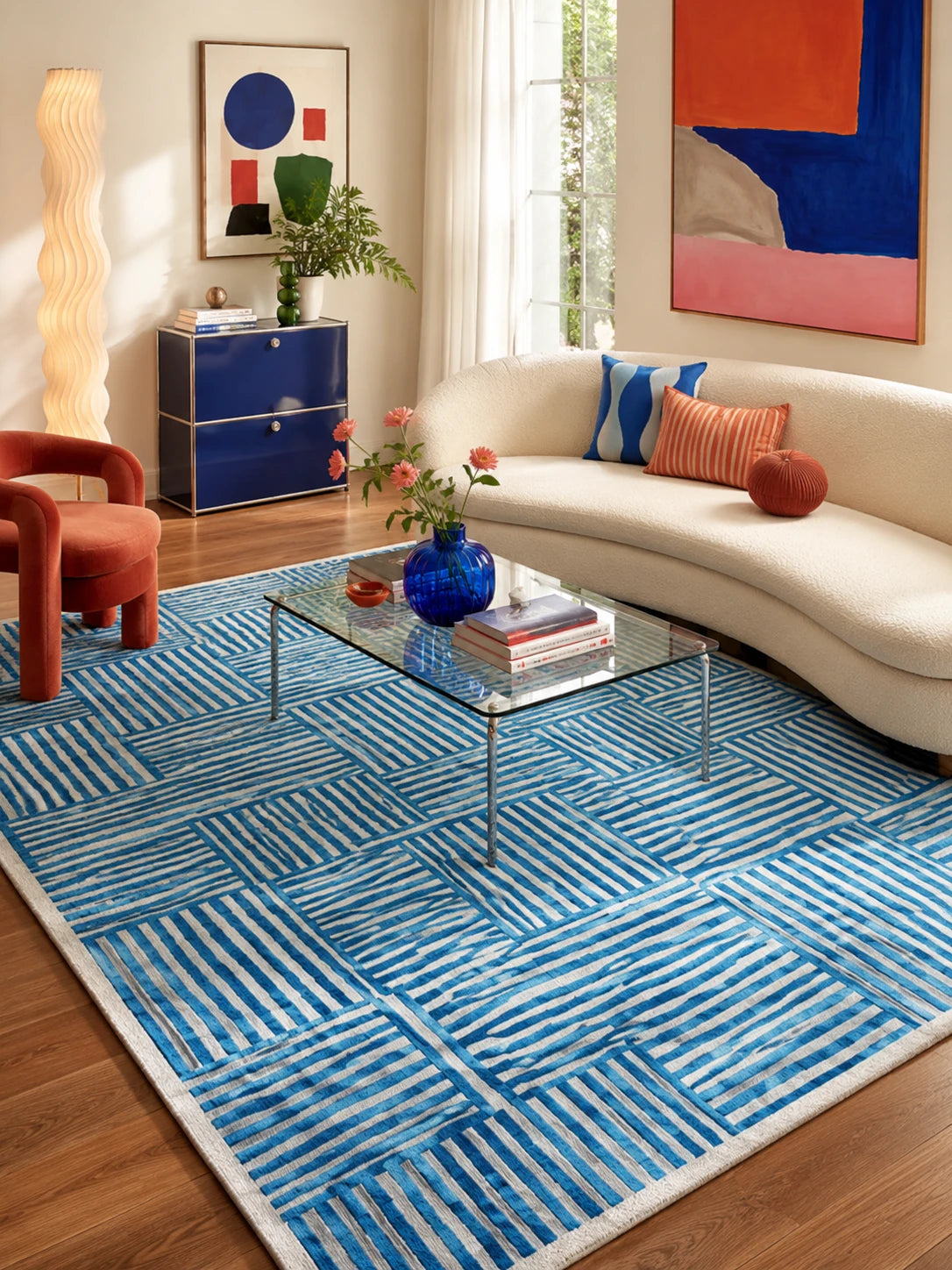 blue stripe patchwork rug under a glass coffee table with a cream curved sofa and rust armchair