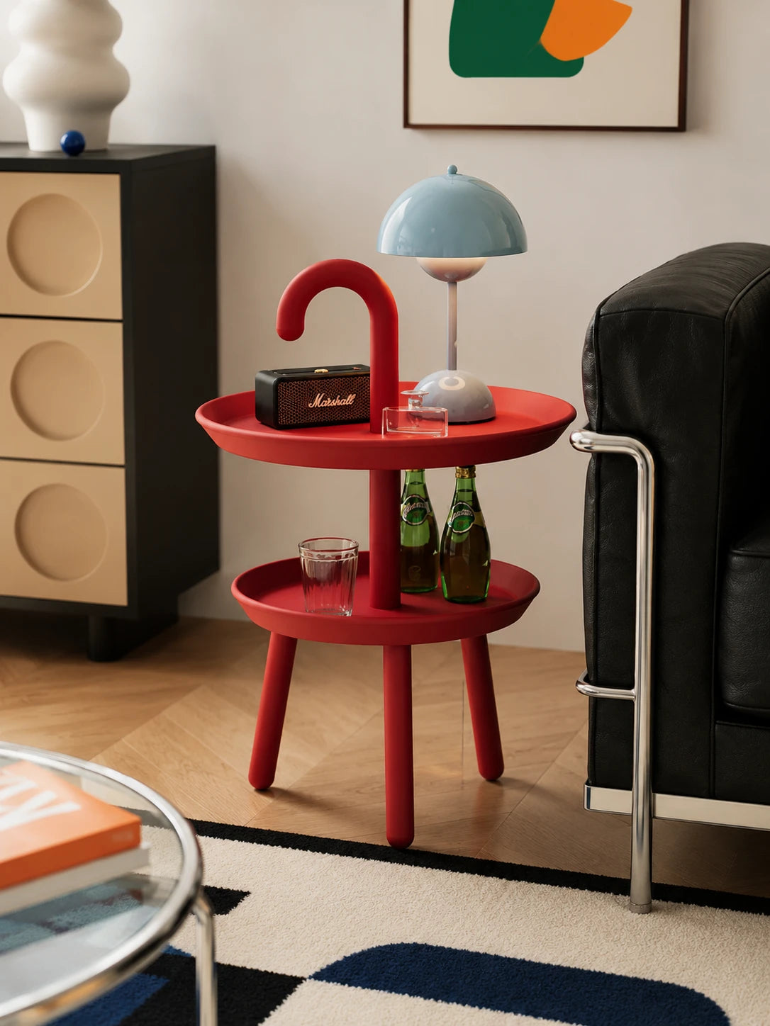 red umbrella-hook side table beside a black leather chair holding a speaker, glasses and a pale blue mushroom lamp
