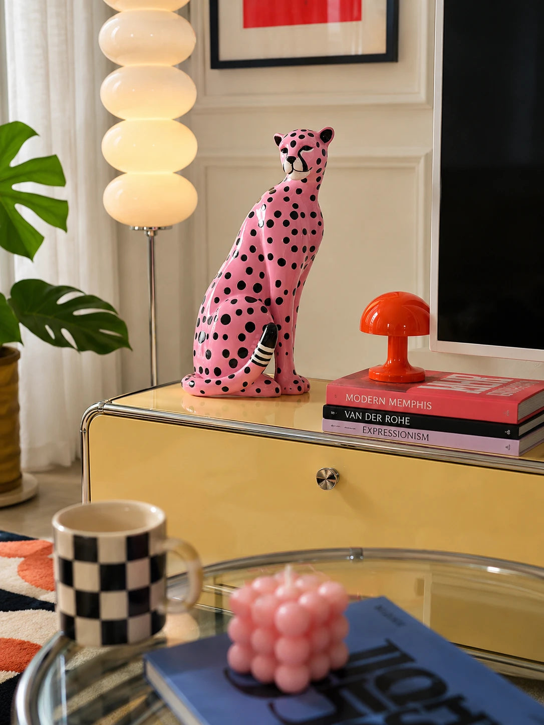 pink spotted leopard figurine on a yellow sideboard next to stacked design books and a small orange lamp