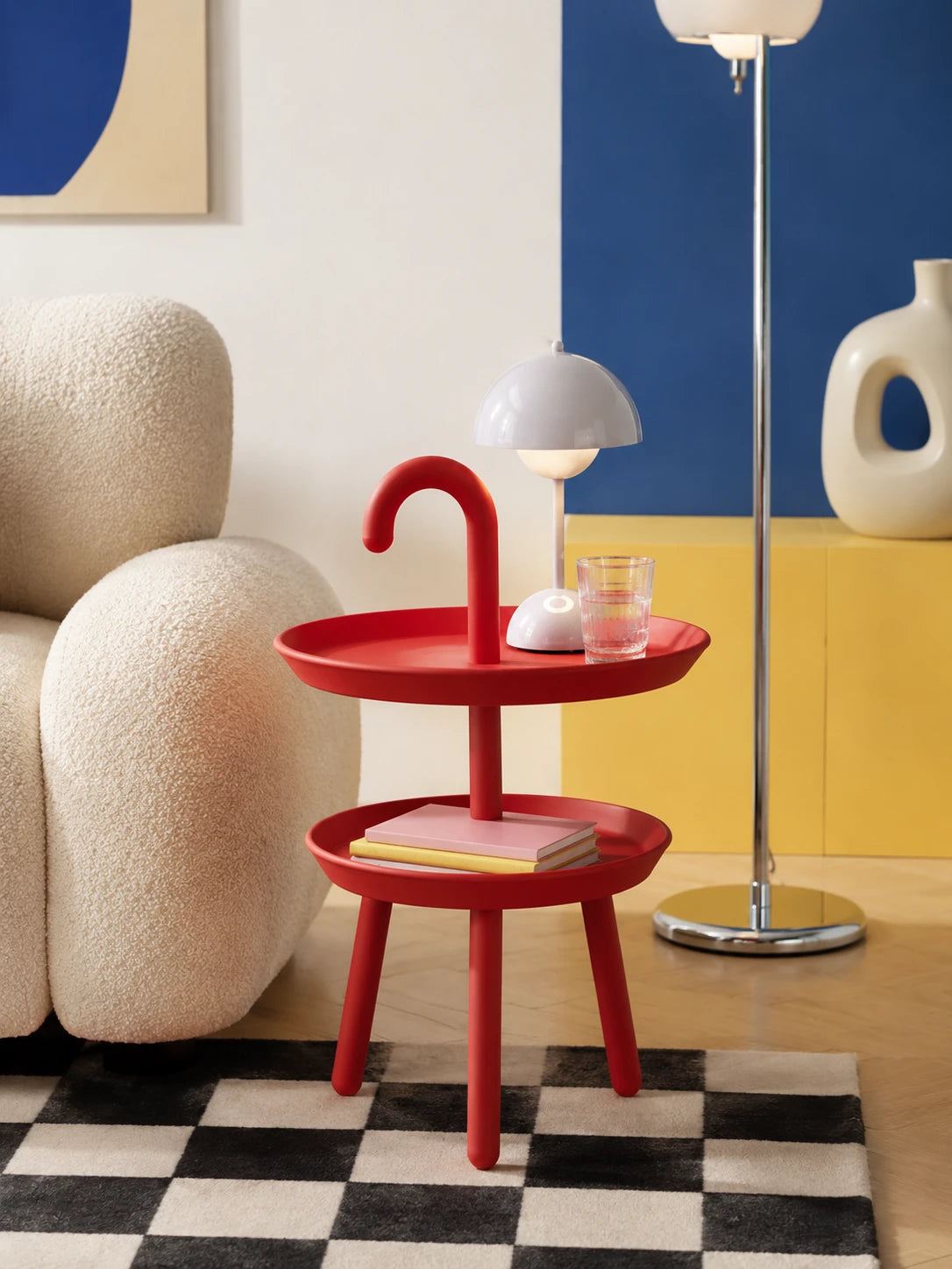 red two-tier hook-handle side table on a checkerboard rug next to a cream boucle sofa with a white mushroom lamp