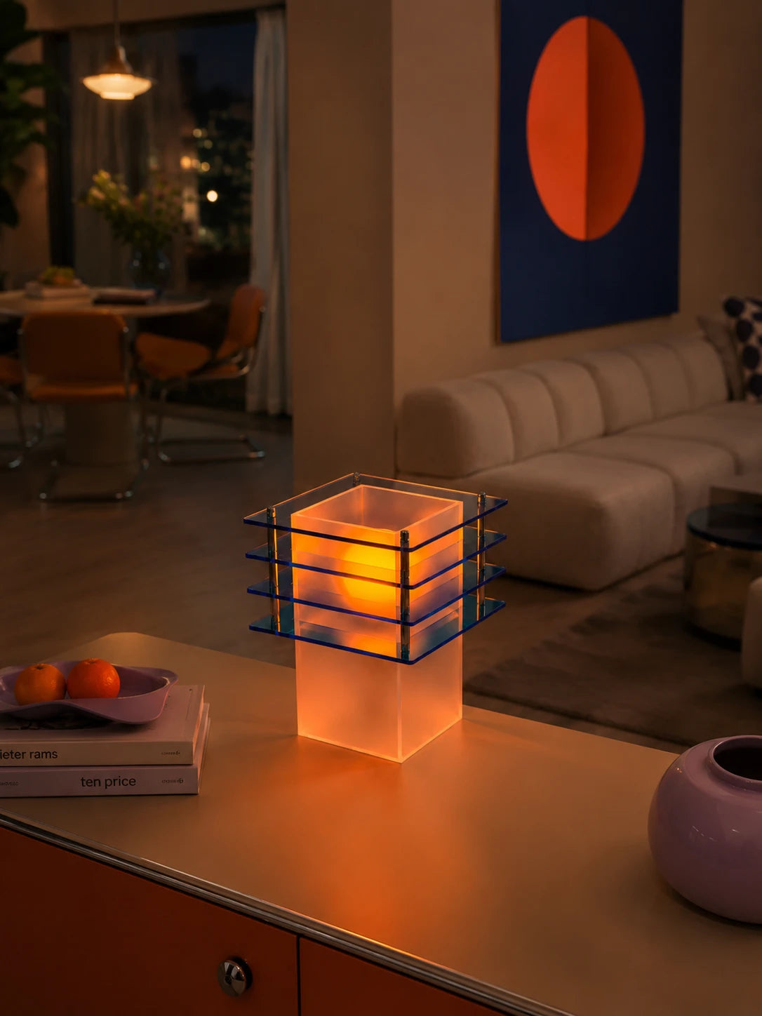 tiered acrylic lamp glowing warm on a sideboard beside stacked books in an evening living room