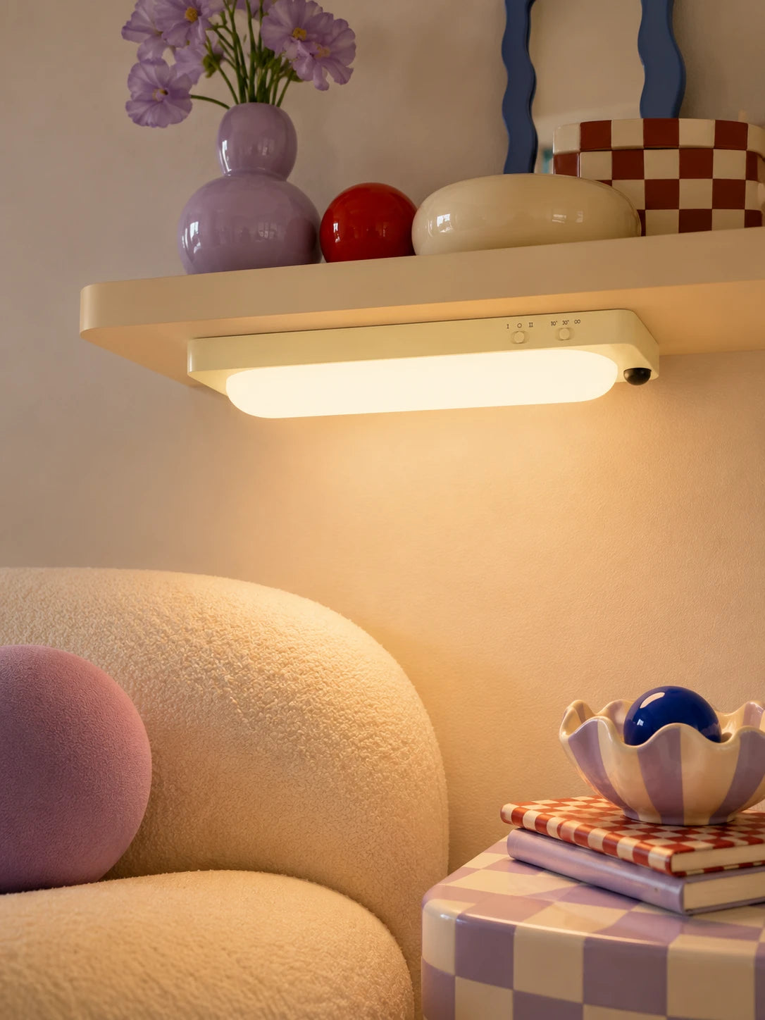 warm-lit motion sensor bar light mounted under a cream shelf above a boucle armchair