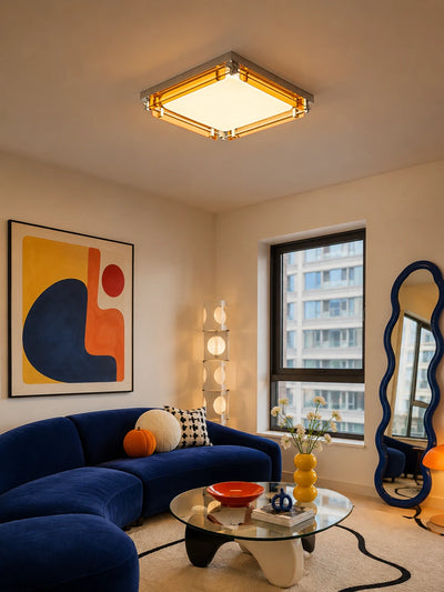 amber acrylic flush mount ceiling light glowing warm above a blue velvet sofa and abstract wall art