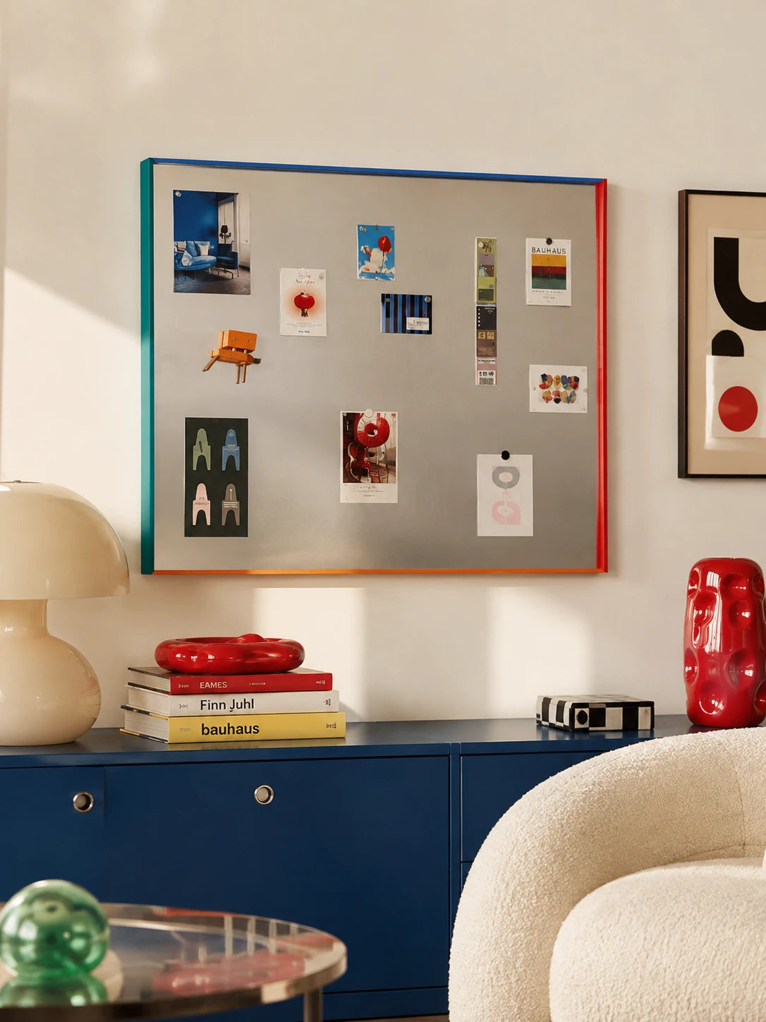 steel magnetic photo board with multicolor frame holding postcards and prints above a navy sideboard
