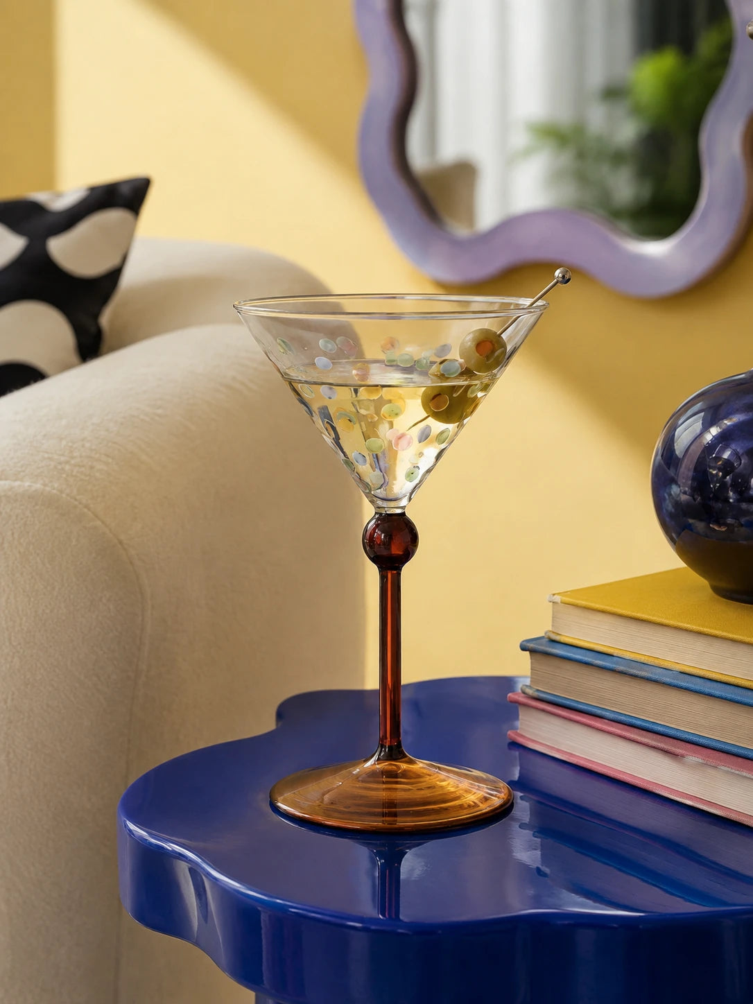 dotted martini glass with olives on a glossy blue scalloped side table beside stacked books