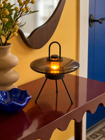 Smoked glass saucer lantern lamp lit warm on a burgundy console under a wavy wood mirror
