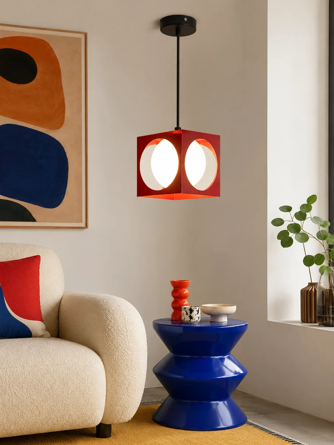 red porthole cube pendant light beside a cream boucle sofa and glossy blue side table