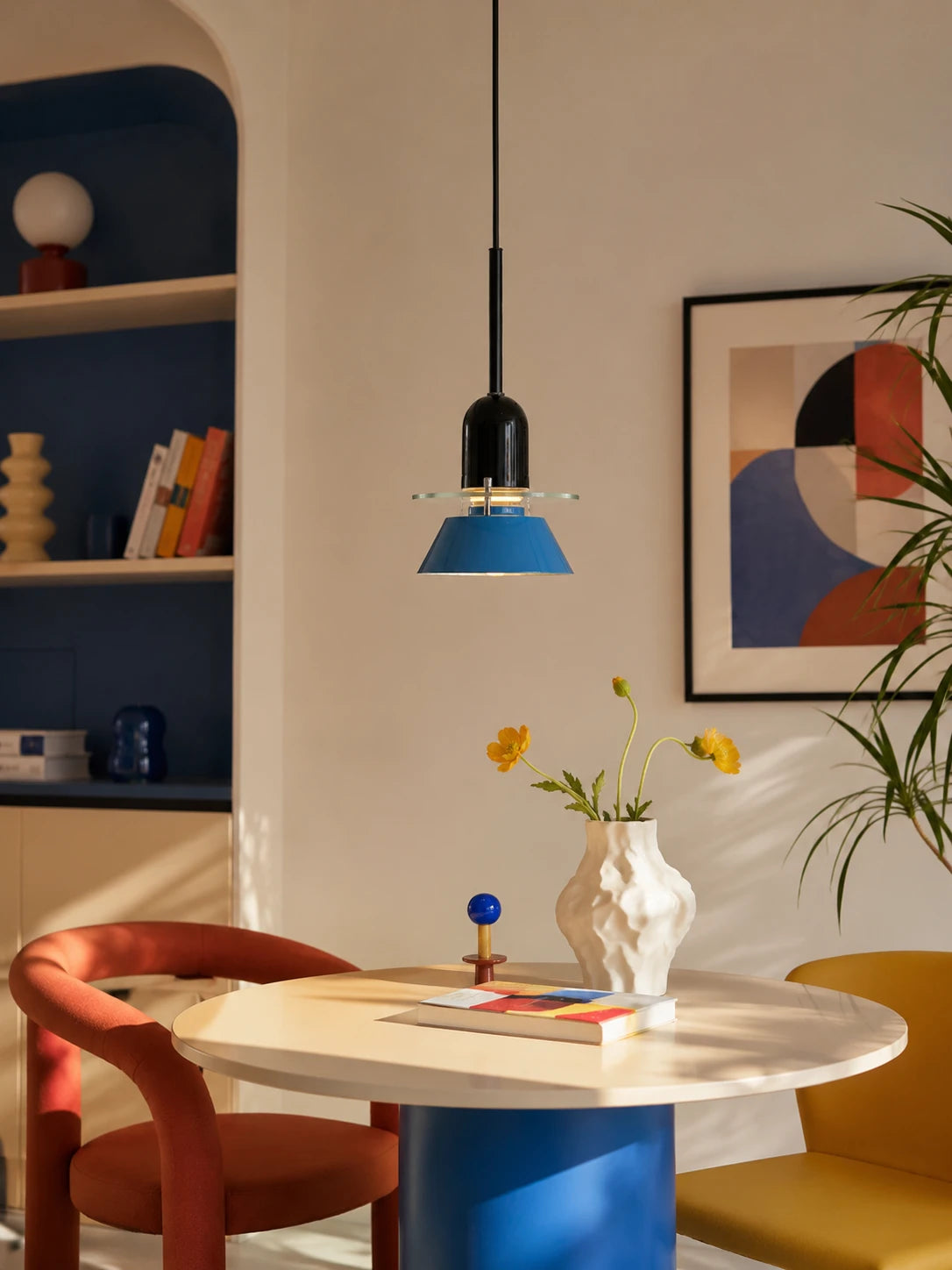 blue cone pendant light hanging over a round dining table with orange and yellow chairs