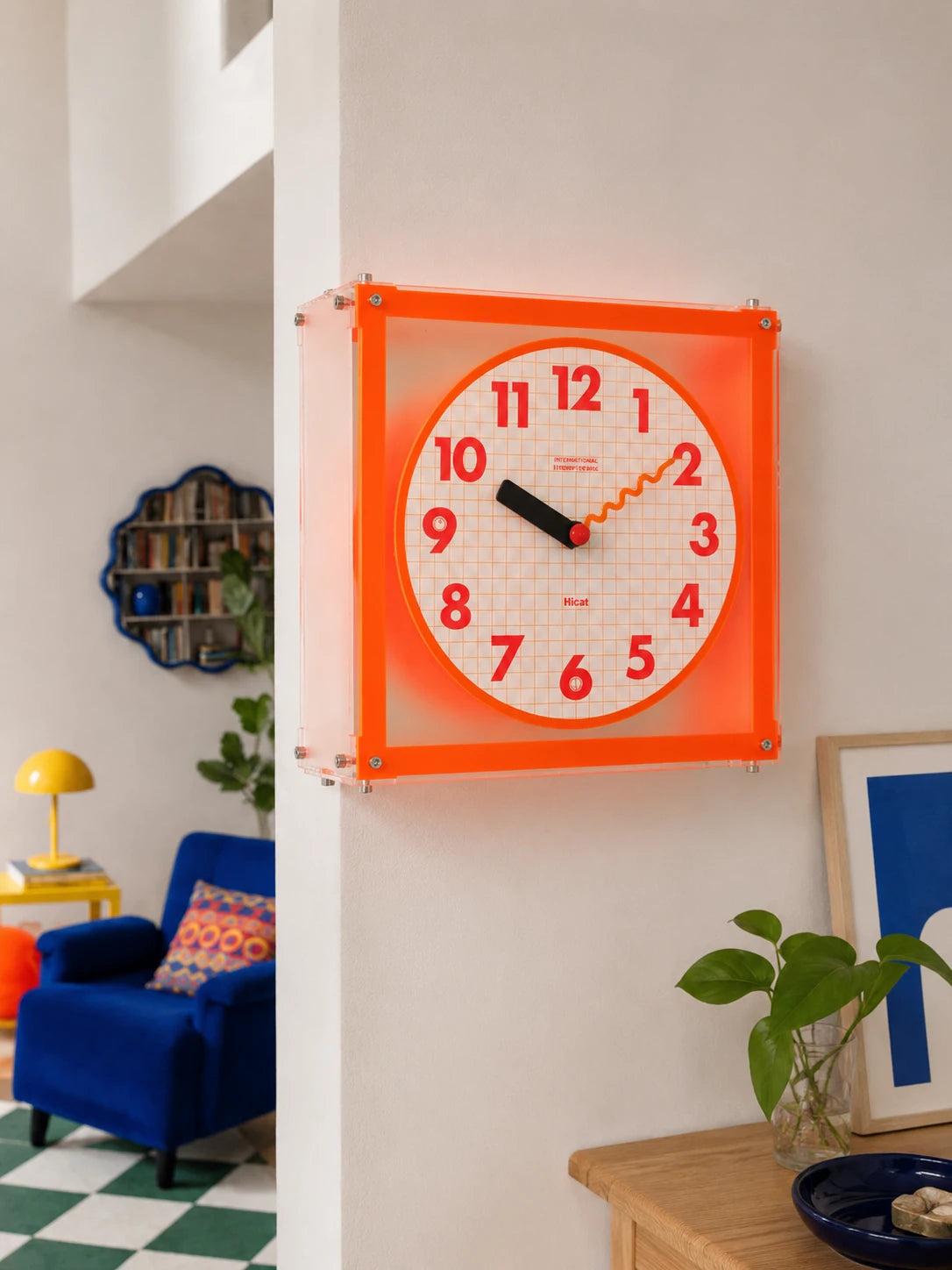 orange acrylic grid clock mounted at a wall corner near a blue armchair and yellow mushroom lamp