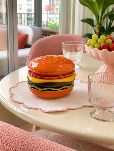 stacked ceramic hamburger plate set on a pink scalloped placemat on a cream dining table with ribbed glasses