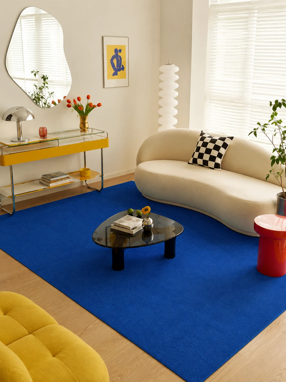 cobalt blue rug under a cream curved sofa and black pebble coffee table in a bright living room