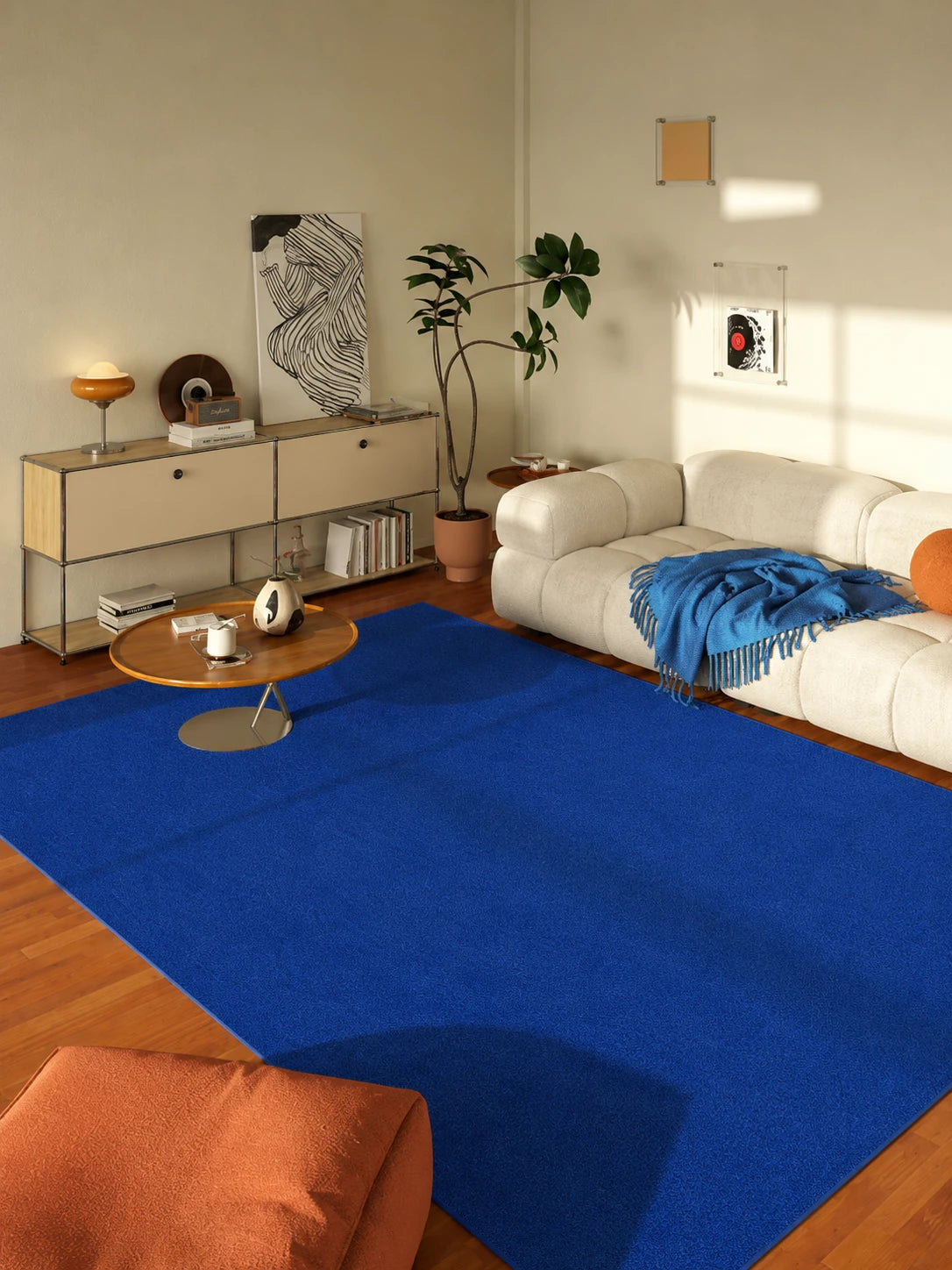 royal blue carpet anchoring a beige tufted sofa and orange armchair in a warm evening living room