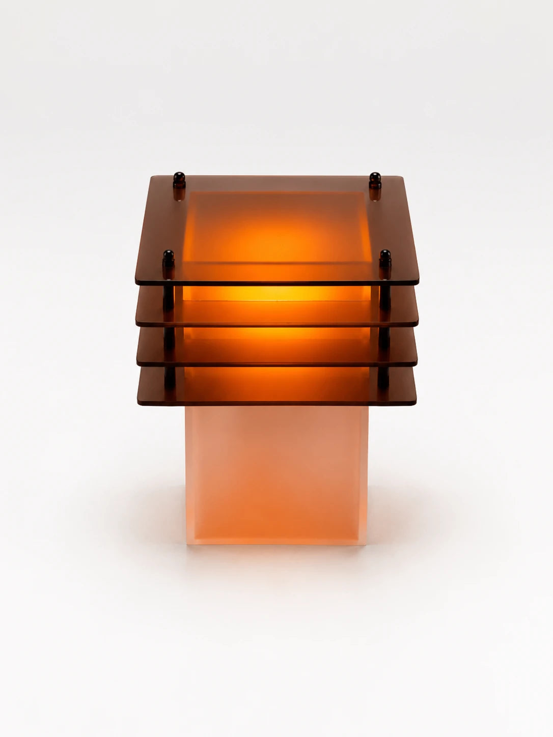 amber-lit tiered acrylic table lamp with four stacked square plates over a glowing frosted column