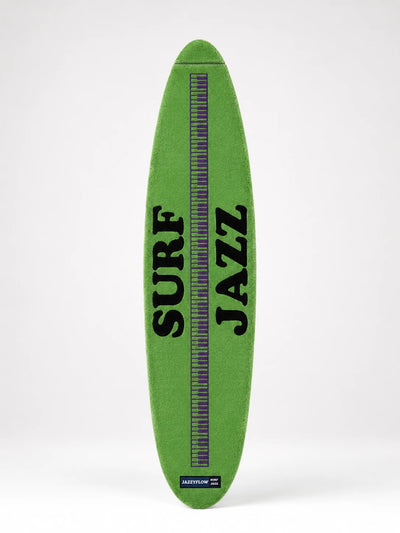 green plush surfboard rug with black lettering and a purple piano-key stripe down the middle