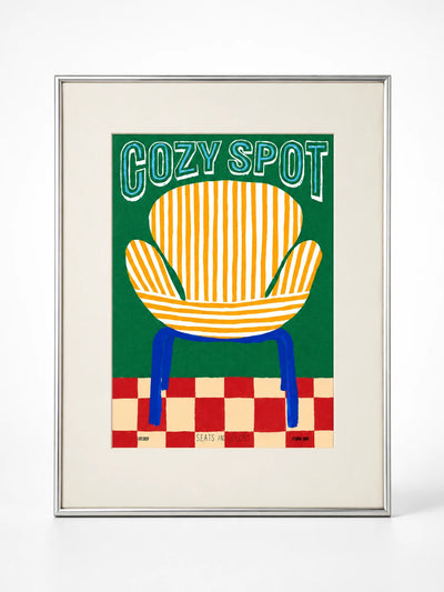 Framed art print of an orange striped armchair on a green background lettered Cozy Spot, silver metal frame