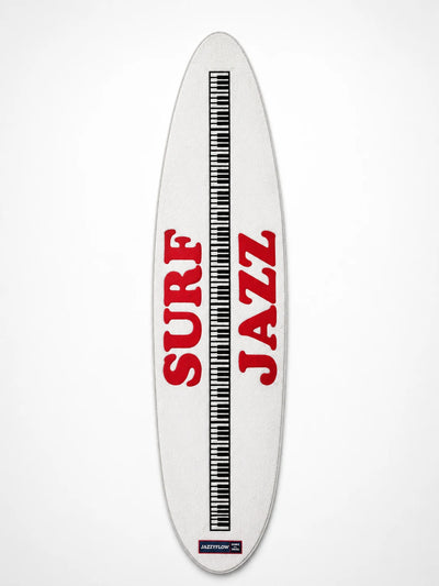white surfboard-shaped plush runner rug with red lettering and a black piano-key stripe down the center