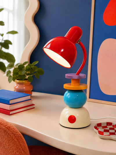 stacked orb Memphis table lamp glowing on a cream desk against a blue wall